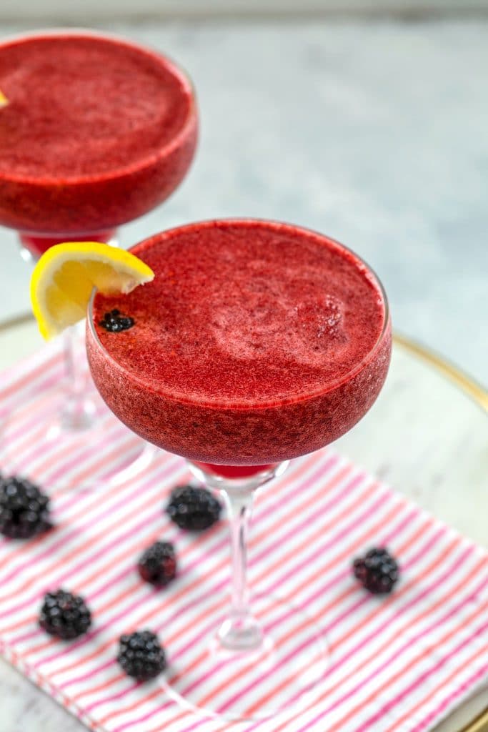 Overhead view of frozen blackberry lemonade margaritas on a pink striped towel with blackberries all around