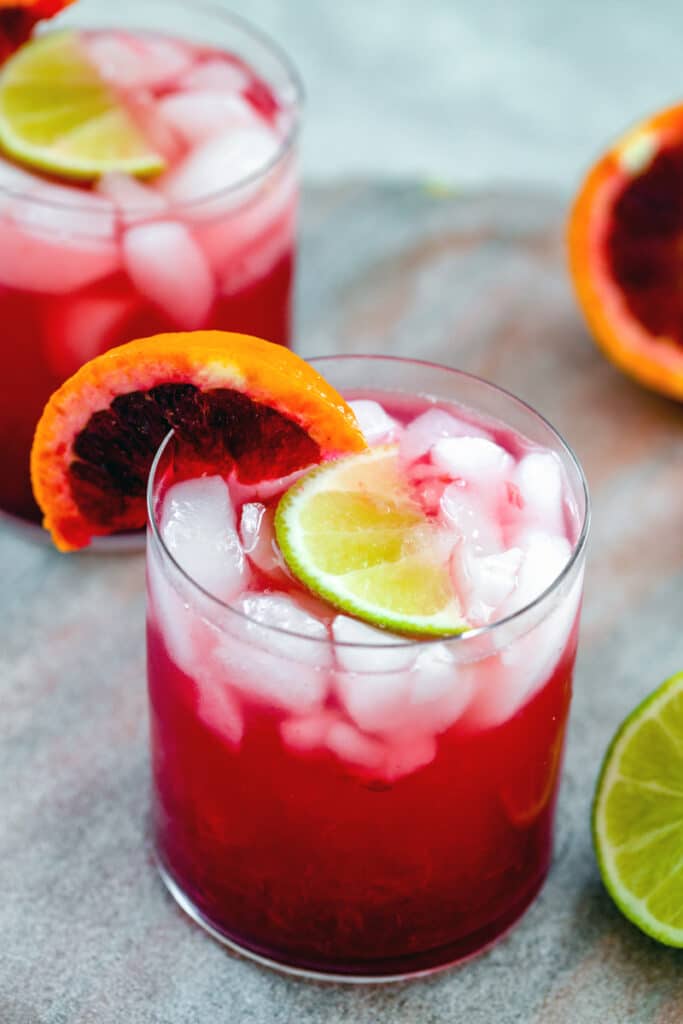 Overhead view of blood orange gin lime rickey cocktail with blood orange and lime wedges and second cocktail in background