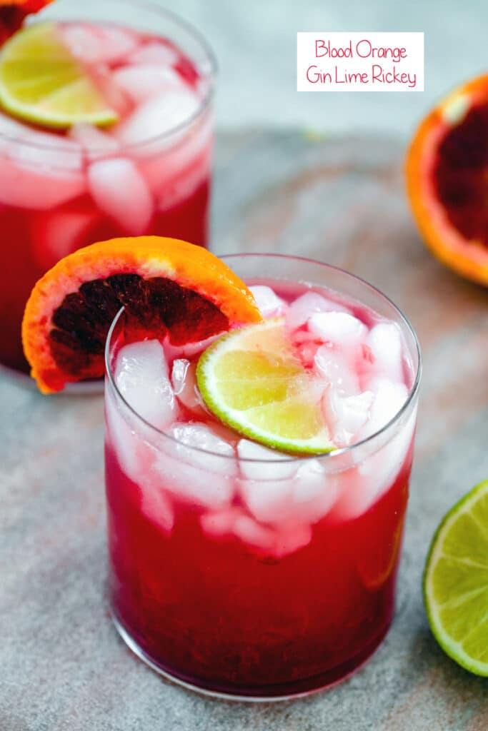 Overhead view of blood orange gin lime rickey cocktail with blood orange and lime wedges and second cocktail in background with recipe title at top