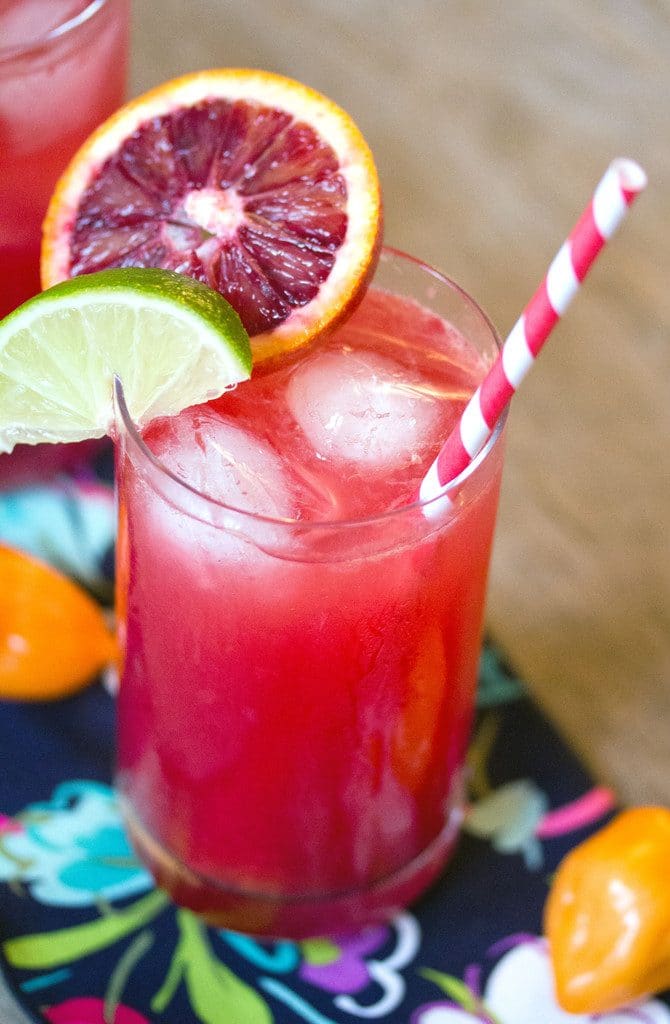 A closeup of the blood orange habanero cocktail with blood orange slice garnish and lime wedge