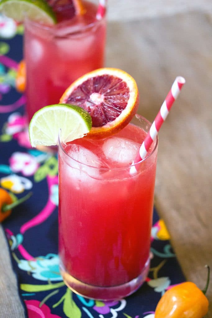 Blood orange habanero cocktail with fruit garnish and a red and white striped straw