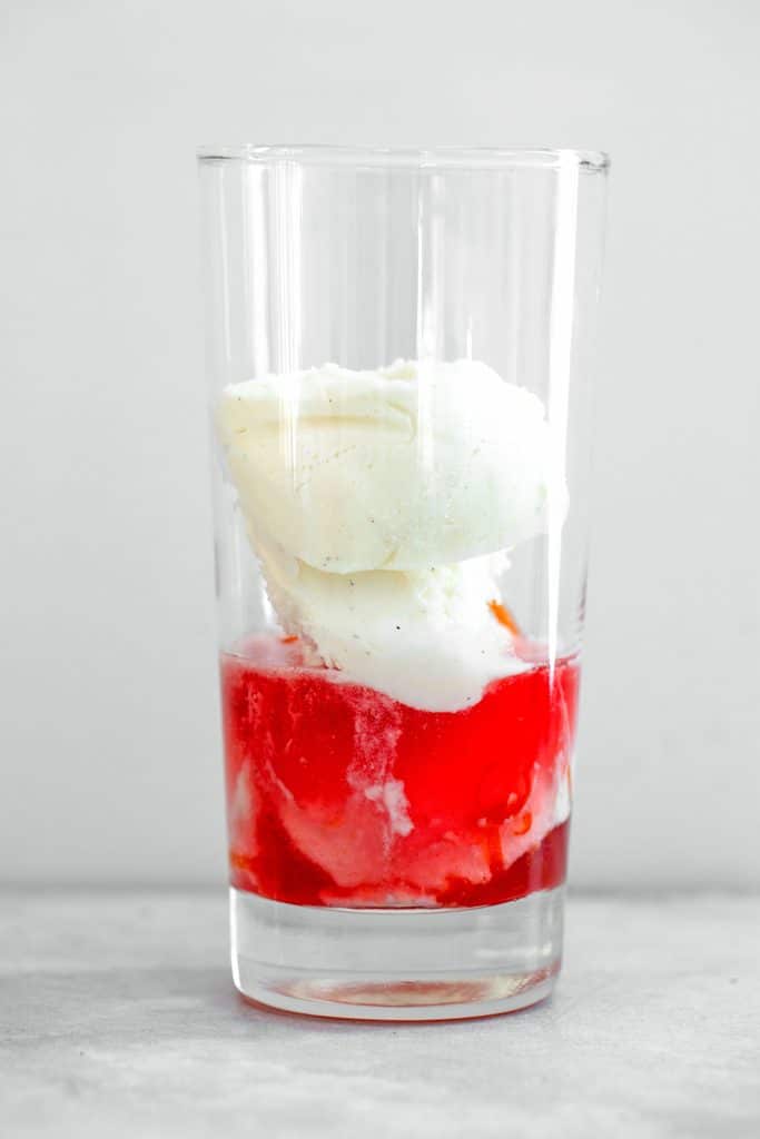 Head-on view of a tall glass filled with vanilla ice cream and blood orange simple syrup