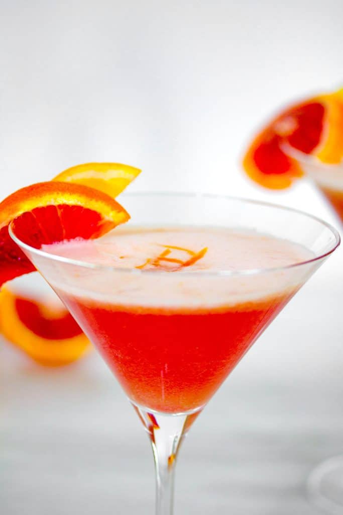 Close-up of the top of a blood orange meyer lemon gin sour in a martini glass with blood orange slice garnish and zest on top