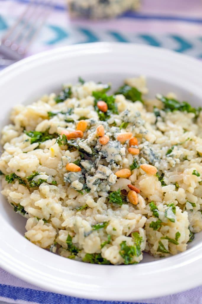 Head-on closeup view of blue cheese risotto with kale topped with crumbled blue cheese and toasted pine nuts