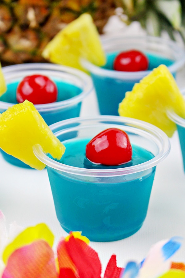 Blue jello shots in little cups with maraschino cherry and pineapple garnish