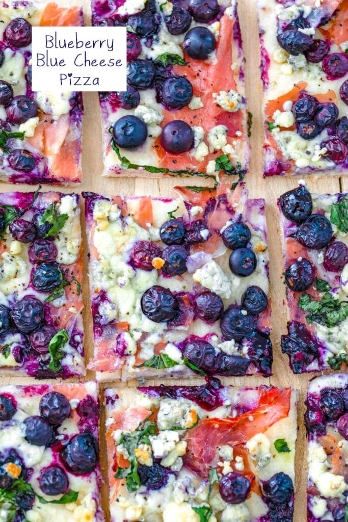 Overhead view of blueberry blue cheese pizza with prosciutto and basil sliced on a cutting board with recipe title at top