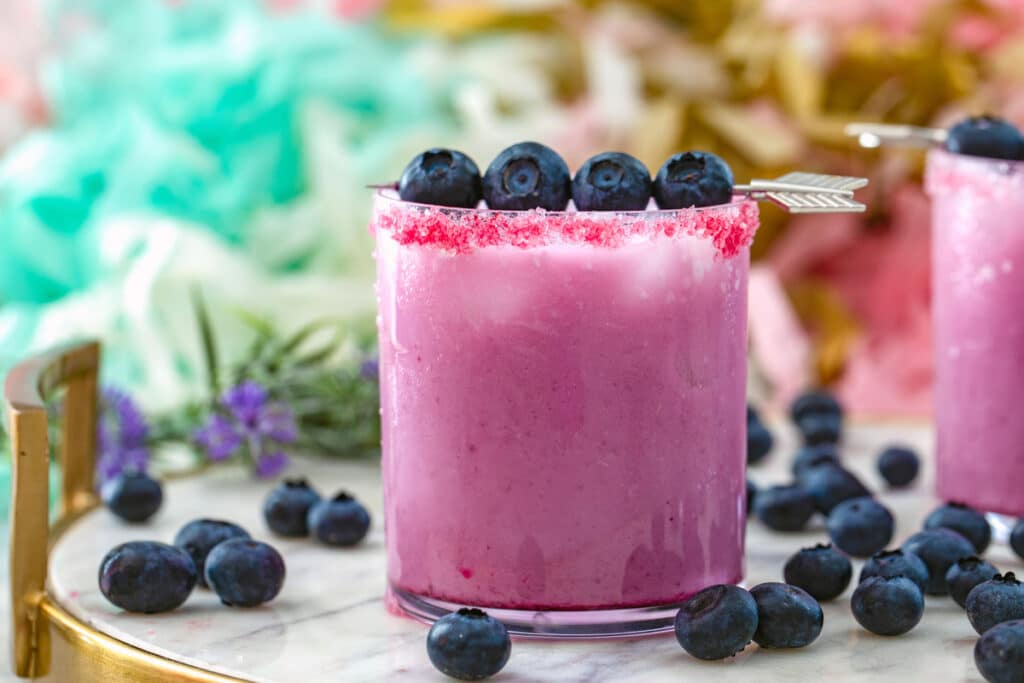 Head-on landscape view of a blueberry coconut margarita on a marble platter with fresh blueberries all around 