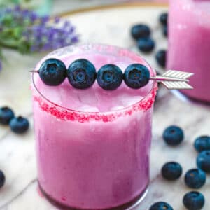 Head-on view of blueberry coconut margarita with blueberry garnish and blueberries all around