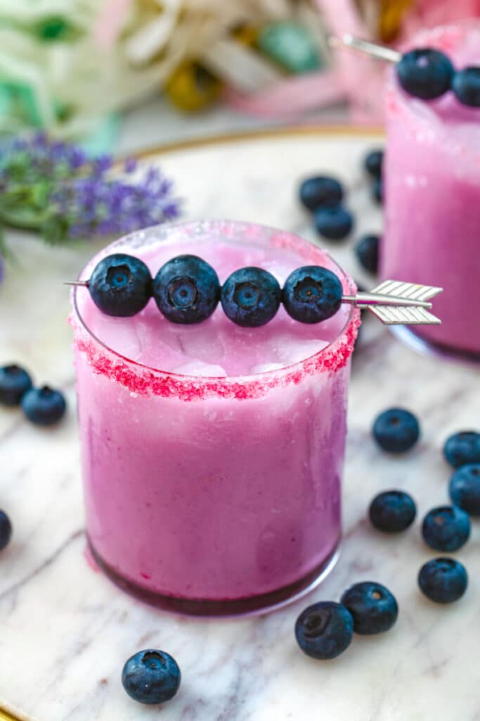 View of a blueberry coconut margarita with fresh blueberry garnish and blueberries in background