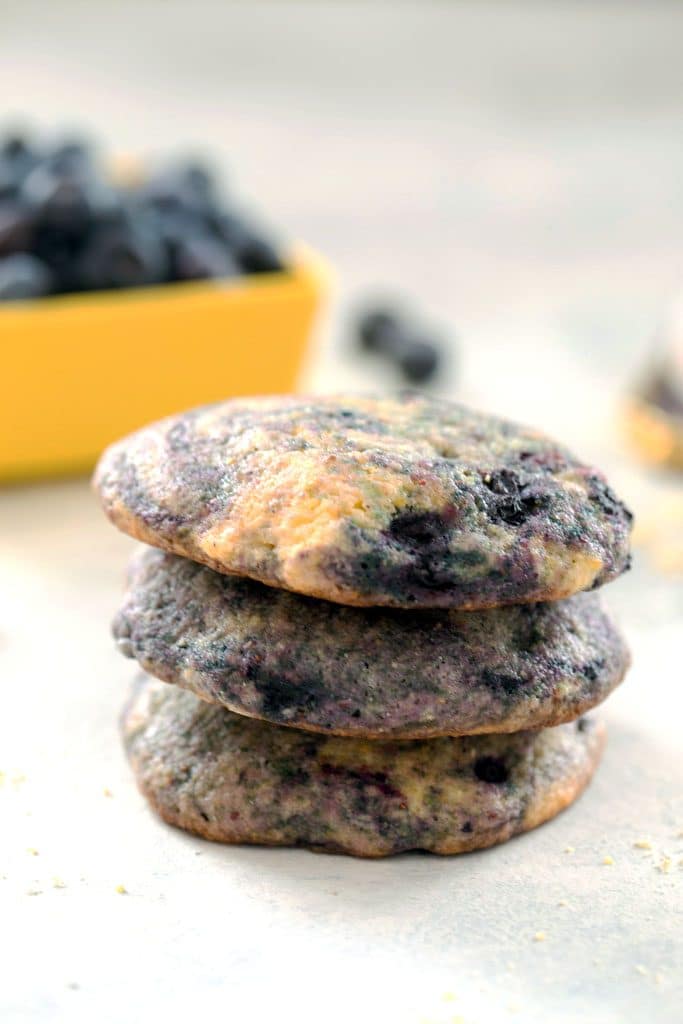 A closeup of three Blueberry Corn Toaster Cakes stacked on top of each other with a bowl of blueberries in the background