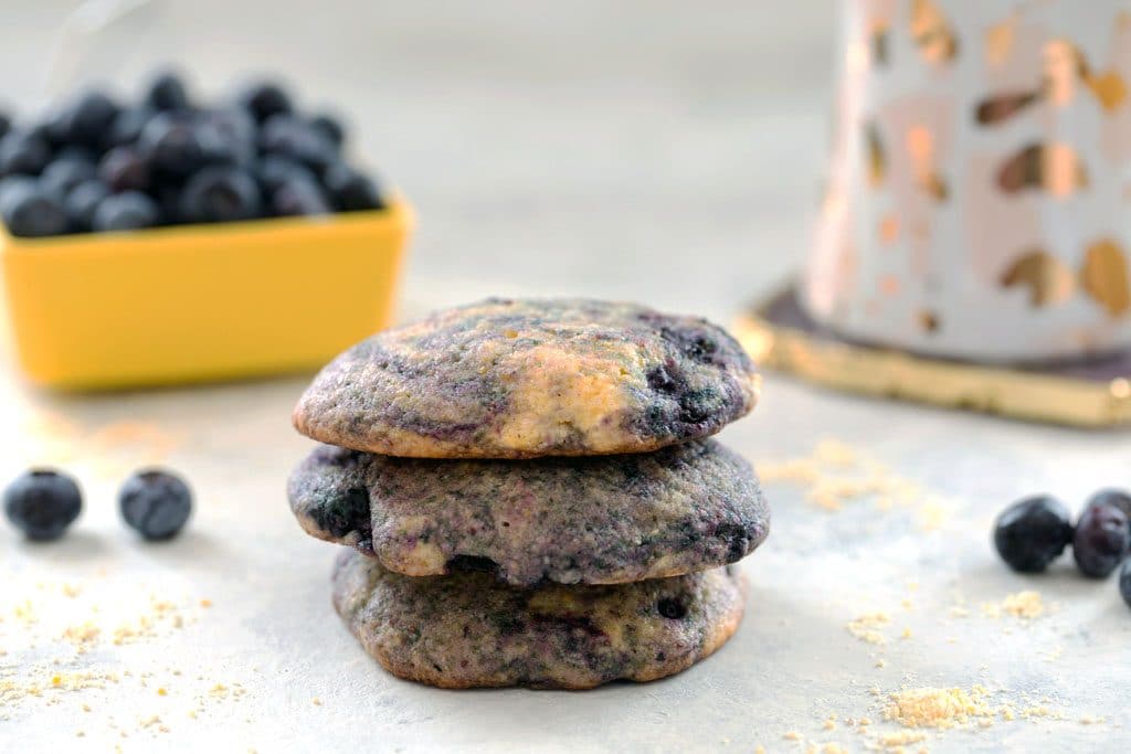 Three Blueberry Corn Toaster Cakes stacked on top of each other with a bowl of blueberries and a coffee cup in the backgrouns