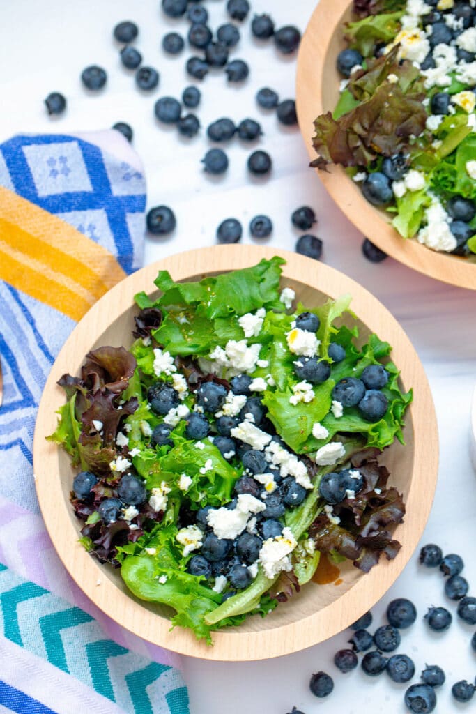 Bird's eye view of blueberry feta salad in a bowl with lettuce with second bowl and blueberries in background