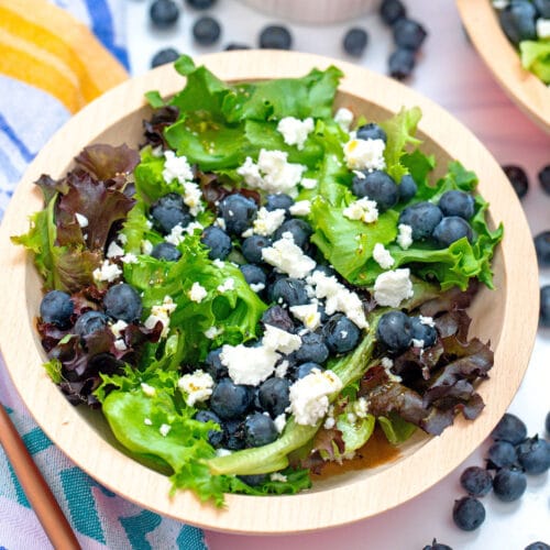 An overhead closeup view of a blueberry and feta salad with mixed greens and blueberries all around