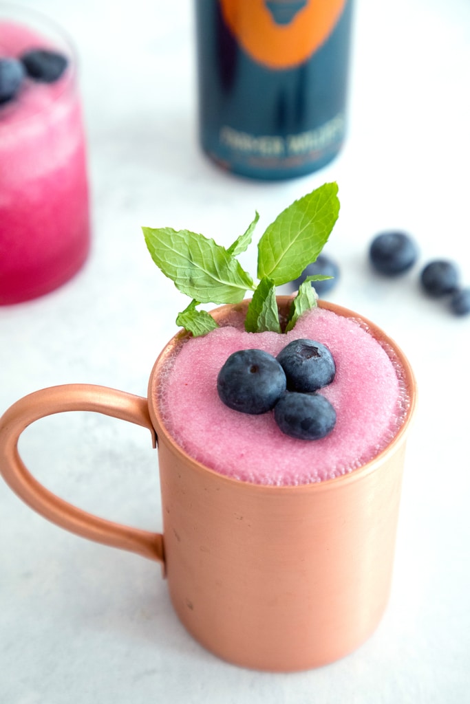 Overhead view of a frozen blueberry moscow mule in a copper mug with blueberries and mint.