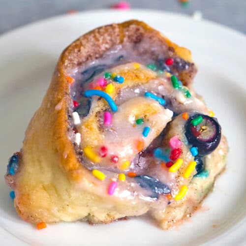 Overhead closeup view of a blueberry funfetti cinnamon roll with fresh blueberries and rainbow sprinkles