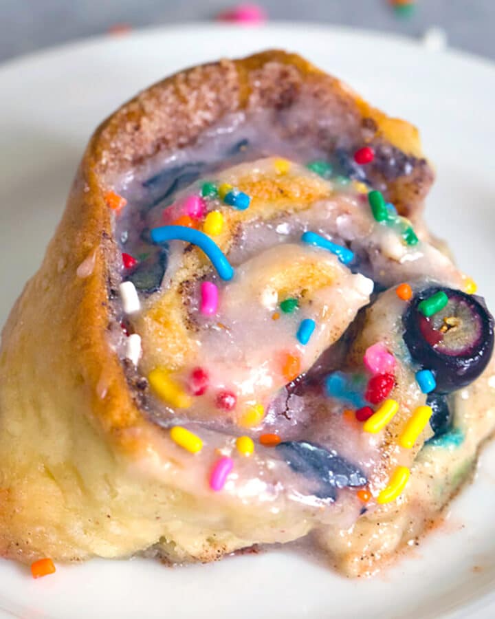 Overhead closeup view of a blueberry funfetti cinnamon roll with fresh blueberries and rainbow sprinkles
