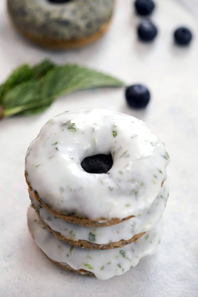 Close-up of a stack of three blueberry mojito doughnuts covered in icing with blueberries and mint in the background