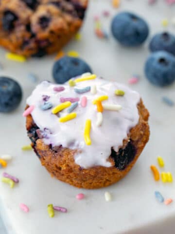 Overhead close-up view of a blueberry muffin for dogs on marble platter with blueberries and sprinkles all around.