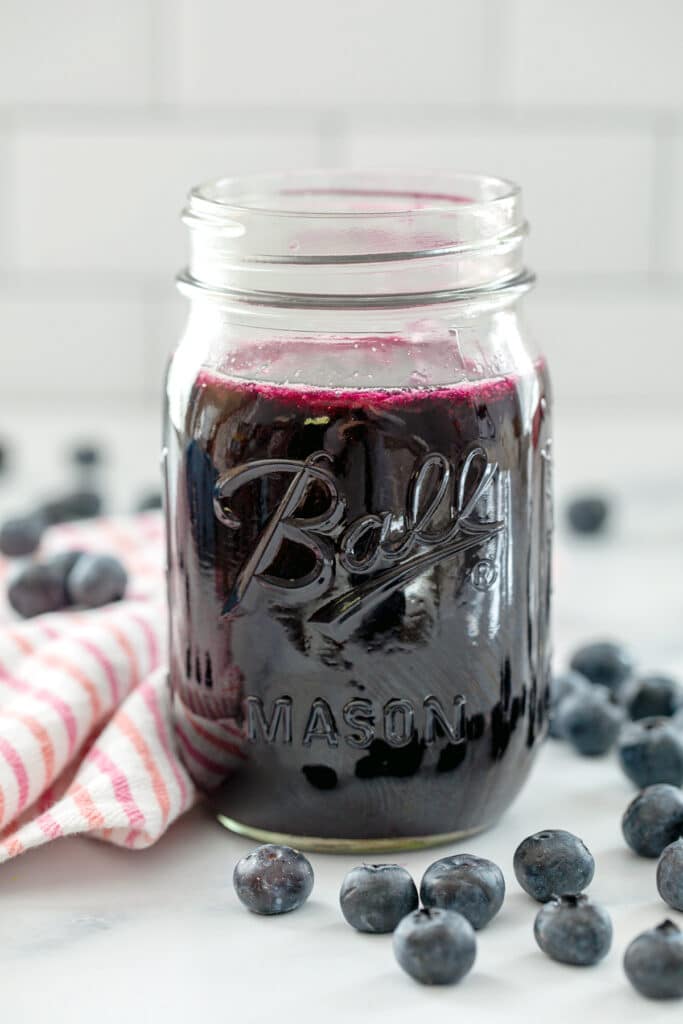 Head-on view of a mason jar of blueberry simple syrup with fresh blueberries all around.