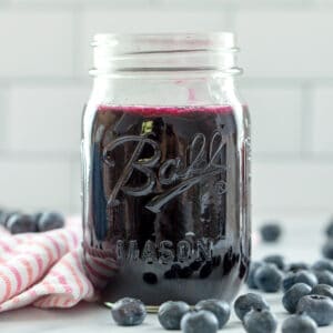 Head-on view of a mason jar of blueberry simple syrup with blueberries all around