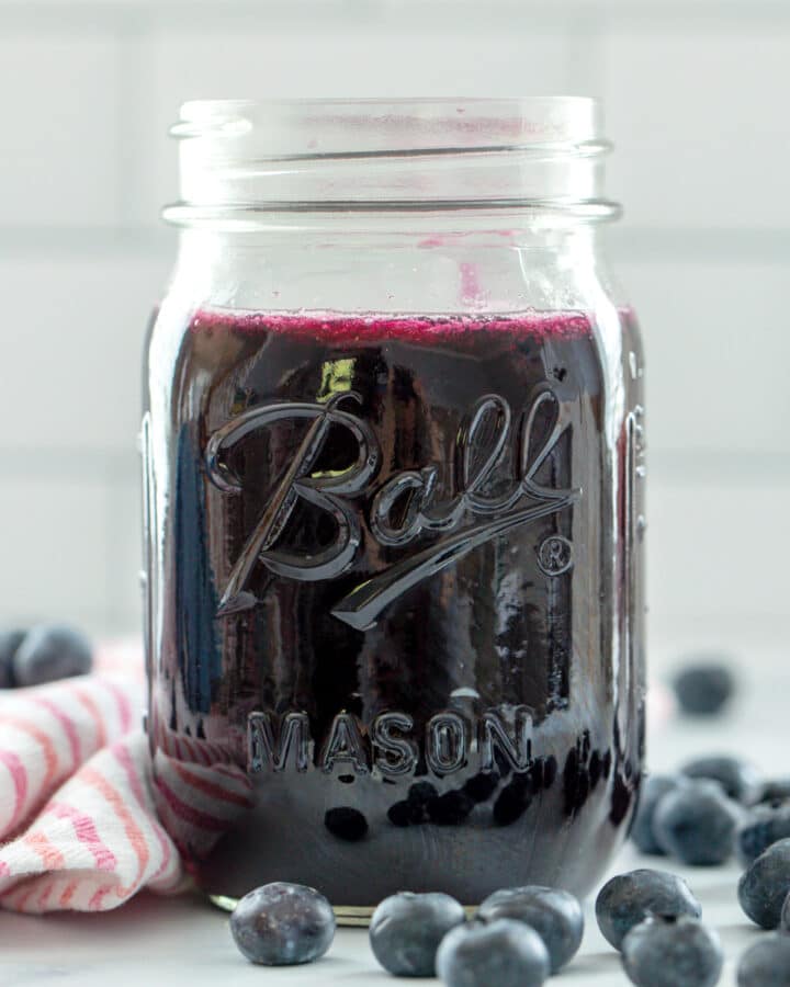 Head-on view of a mason jar of blueberry simple syrup with blueberries all around