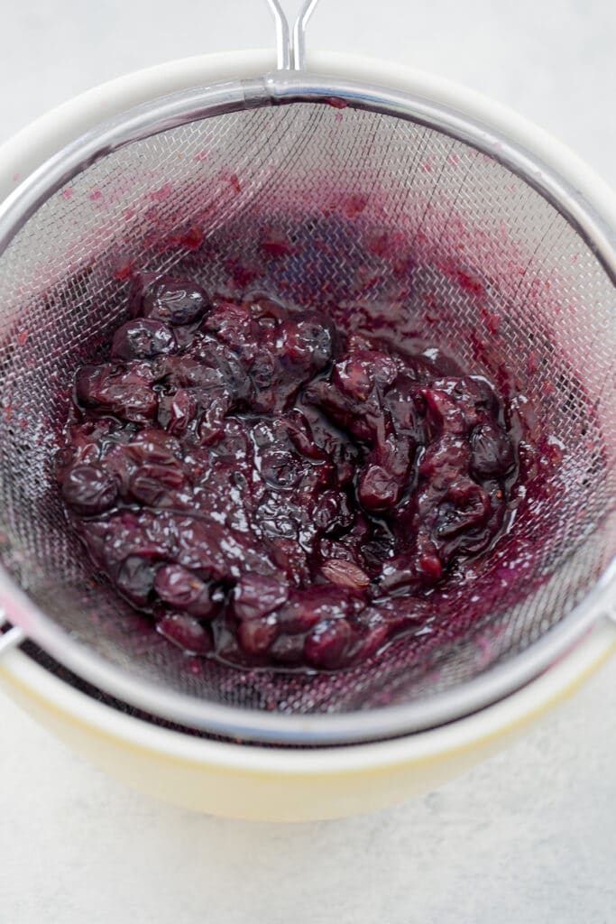 Blueberries being strained out of simple syrup over bowl.