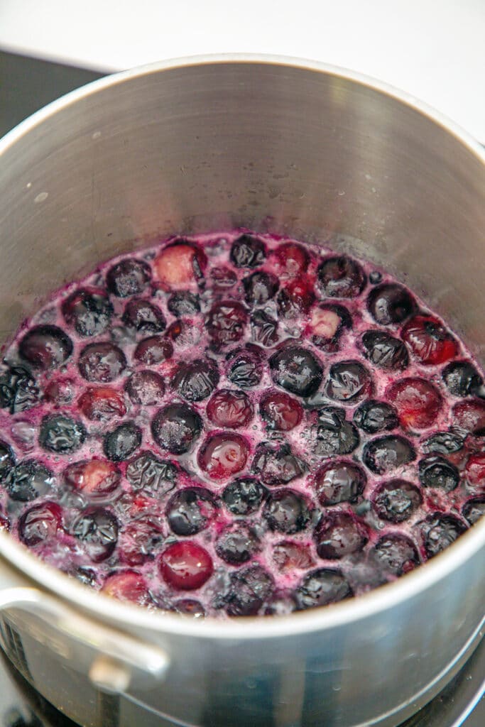 Blueberries simmering in water and sugar in saucepan.