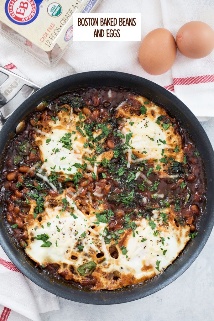 Overhead view of a skillet with Boston baked beans and eggs topped with parsley with whole eggs in the background and recipe title at top