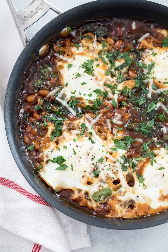 Overhead close-up view of a skillet with Boston baked beans and eggs topped with chopped parsley