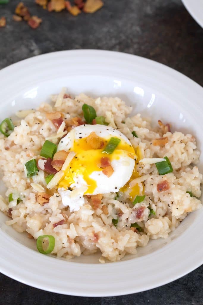 Overhead closeup view of breakfast risotto in bowl with runny poached egg on top and bacon, cheese, and scallions mixed in