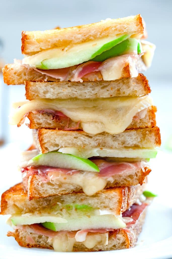 Close-up head-on photo of four halves of a brie grilled cheese sandwich with fig spread, green apple and prosciutto stacked on top of each other