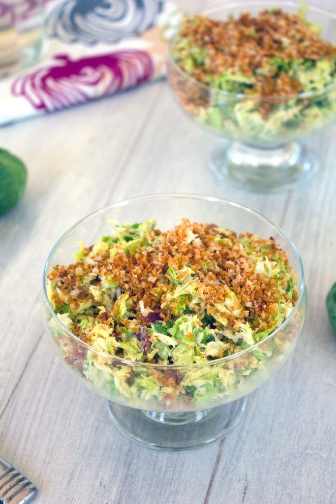 View of bowl of brussels sprouts bacon caesar salad topped with panko with second bowl in background