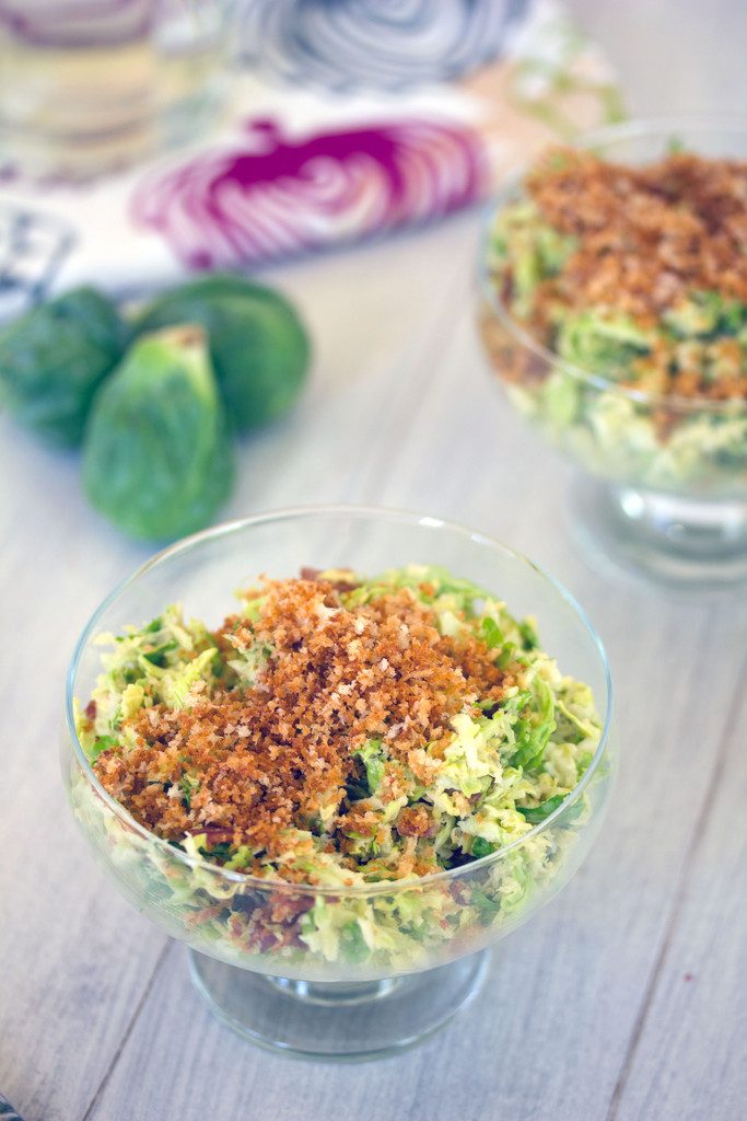 Close-up view of brussels sprouts caesar salad topped with panko with second bowl and brussels sprouts in background