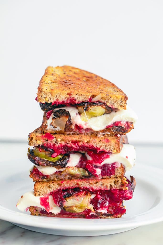 Head-on view of three brussels sprouts and cranberry relish grilled cheese stacked on each other on a white plate