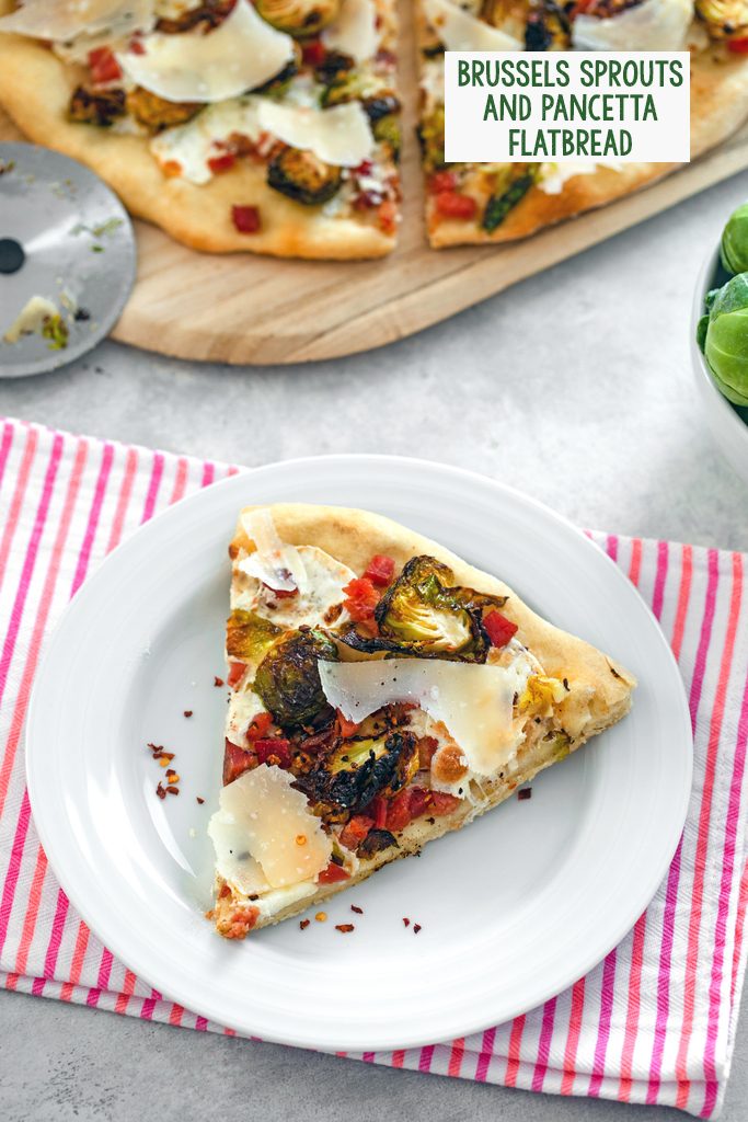 Overhead view of a slice of brussels sprouts flatbread with pancetta and parmesan on a white plate with rest of pizza and pizza cutter in background with recipe title at top