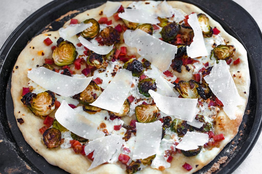 Landscape overhead view of brussels sprouts and pancetta flatbread just out of the oven and topped with shaved parmesan cheese