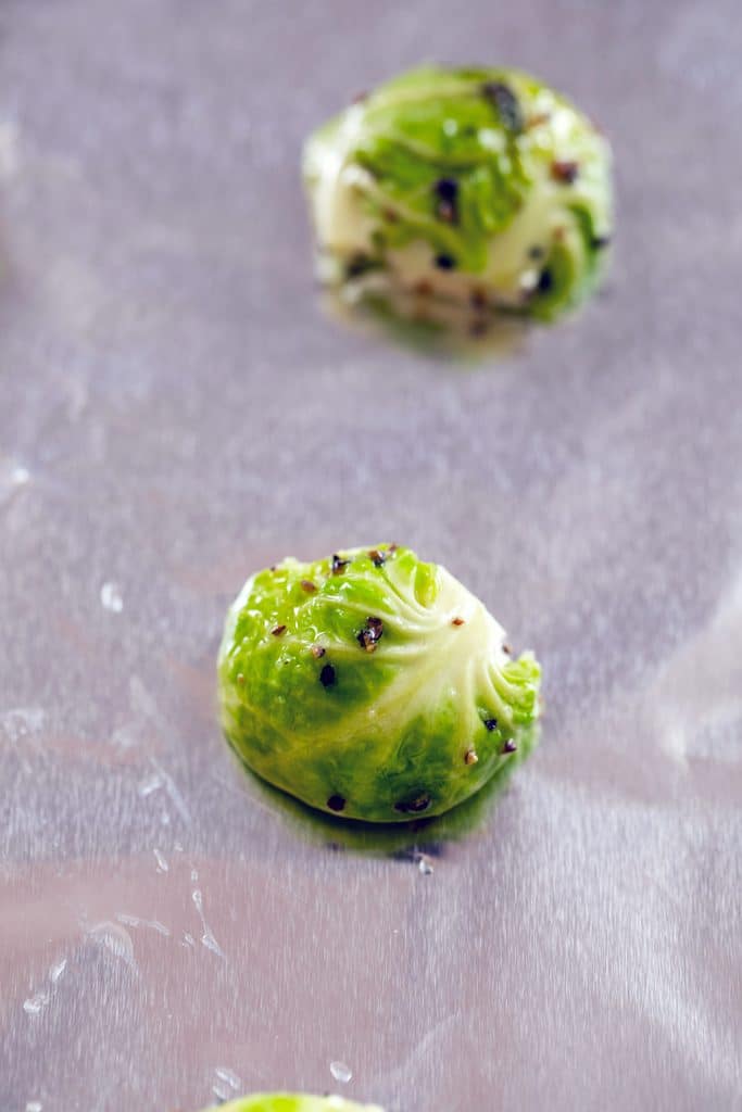 Close-up of raw brussels sprouts halves with salt and pepper on foil-lined baking sheet