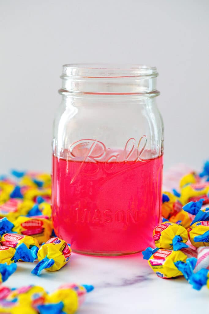 Head-on view of mason jar of pink bubblegum simple syrup with pieces of Double Bubble all around.