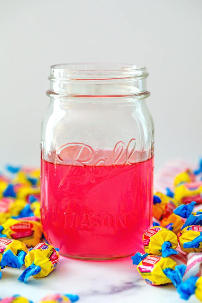 Head-on view of a jar of pink bubblegum simple syrup with Double Bubble gum all around