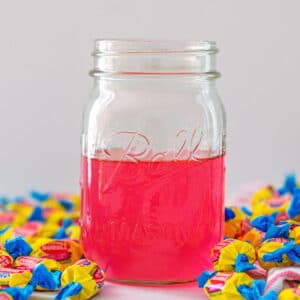 Head-on closeup view of a jar of pink bubblegum simple syrup with Double Bubble gum all around