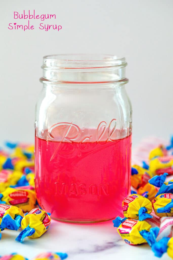 Head-on view of a jar of pink bubblegum simple syrup with Double Bubble gum all around and recipe title at top.