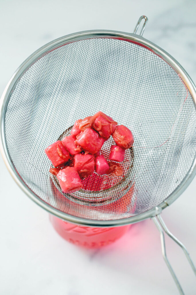 Pieces of bubblegum being strained out of simple syrup into jar.