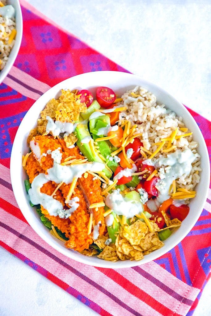 Overhead view of buffalo chicken burrito bowl salad with baked buffalo chicken, avocado, tomatoes, brown rice, shredded cheddar, tortilla chips, and blue cheese dressing