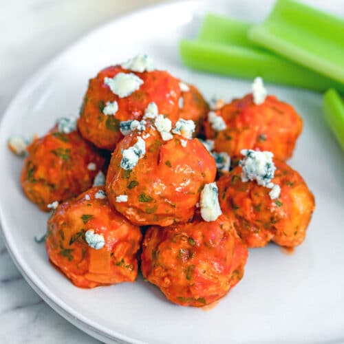 Overhead closeup view of buffalo chicken meatballs topped with blue cheese and served with celery sticks in the background.