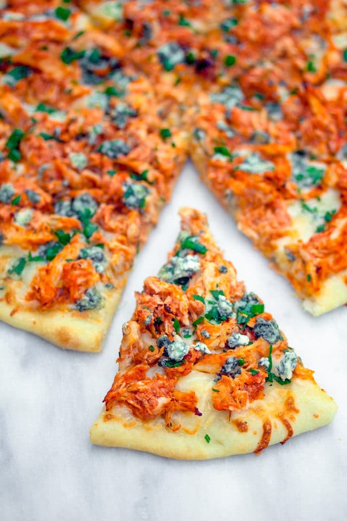 Bird's eye view of a buffalo chicken pizza on a marble surface with a slice of pizza pulled out