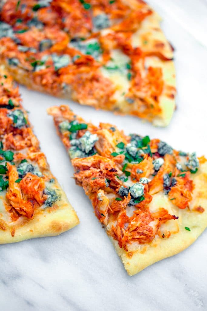 Overhead view of a slice of buffalo chicken pizza pulled out from the rest of the pizza on a marble surface