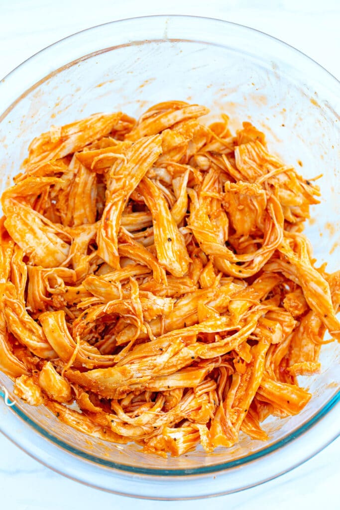Shredded chicken breast in bowl with buffalo sauce