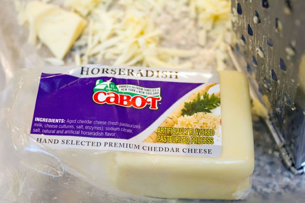 View of Cabot Horseradish Cheddar Cheese block next to a grater and shredded cheese
