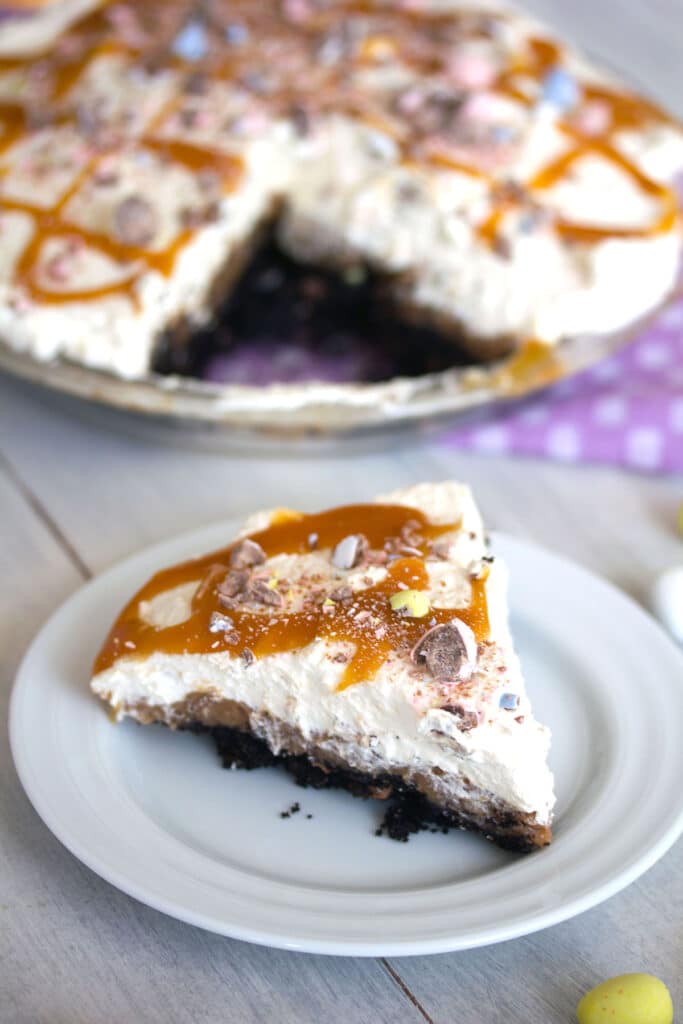 Head-on view of a slice of Cadbury Egg Pie on a white plate with the rest of the pie in the background.