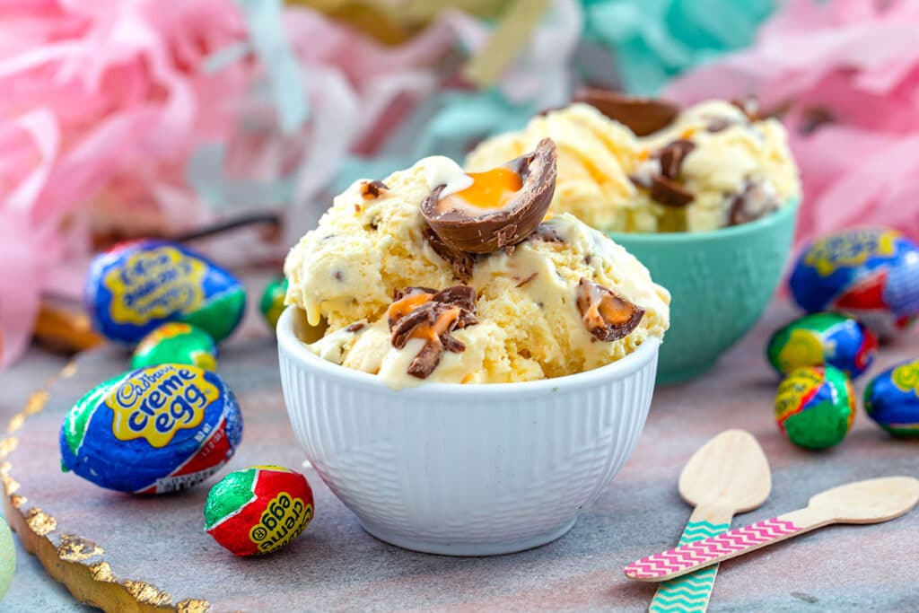 Landscape head-on view of two bowl of Cadbury Creme Egg Ice Cream surrounded by wrapped Cadbury Eggs and wooden spoons